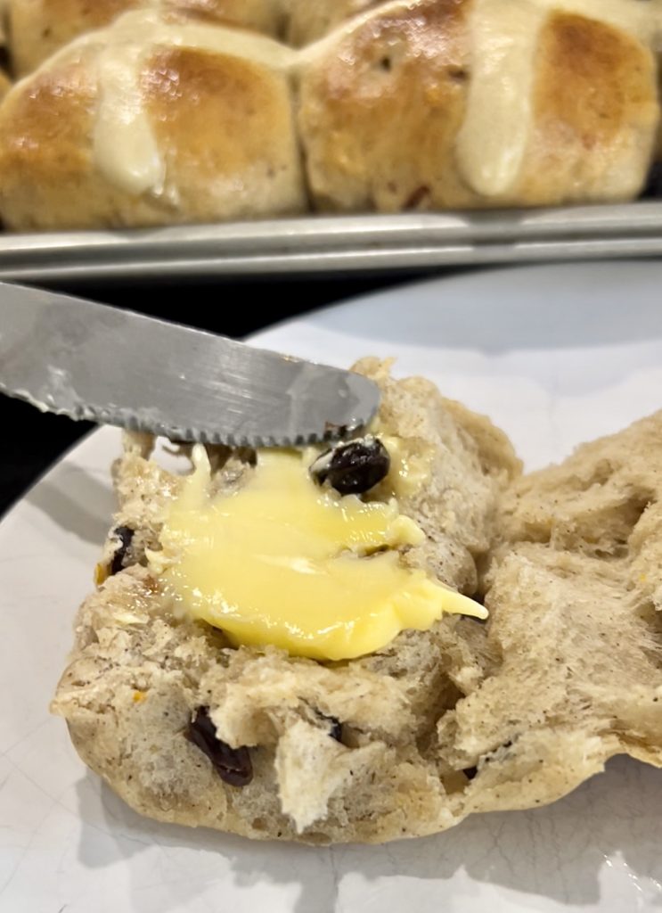 adding butter on to one piece of hot cross bun 