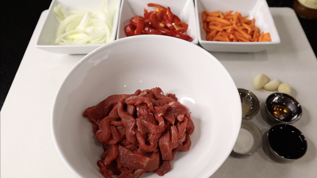 Sliced onion, bell pepper, carrot, strip beef in a separate bawl. 3 garlic cloves. Soy sauce, sesame oil, sugar and white pepper powder in a small container. 