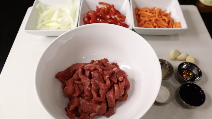 Sliced onion, bell pepper, carrot, strip beef in a separate bawl. 3 garlic cloves. Soy sauce, sesame oil, sugar and white pepper powder in a small container.