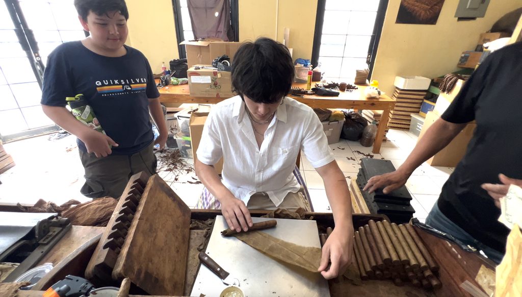Two people rolling cigars at a workbench in a cigar factory