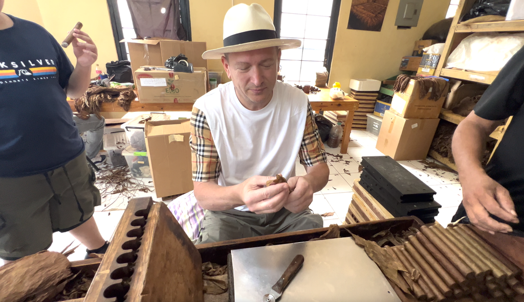 Man in a straw hat rolling a cigar at a cigar factory workbench