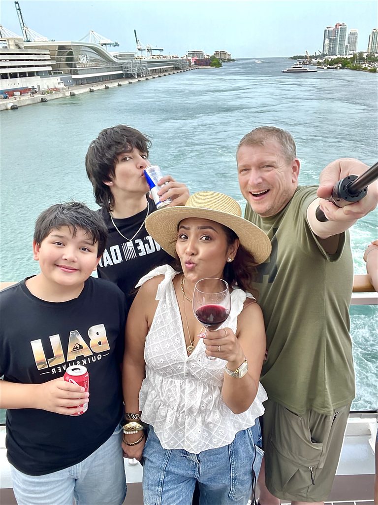 Family of four smiling on the ship's deck with the Miami port behind them