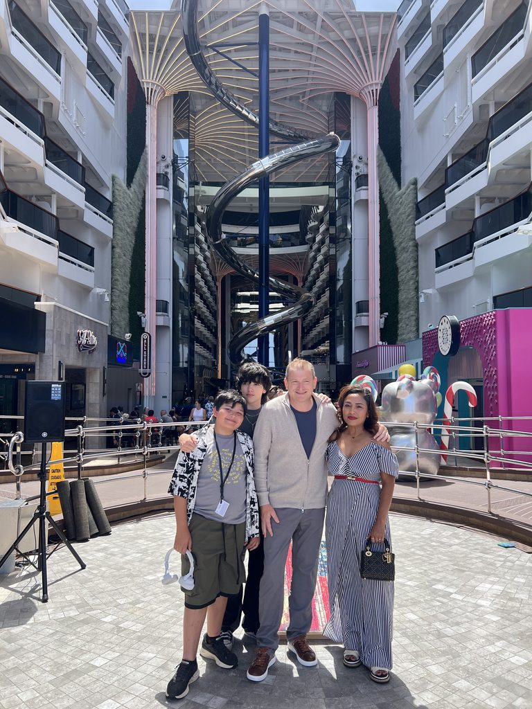 Family of four standing in the ship's atrium with a spiral slide above