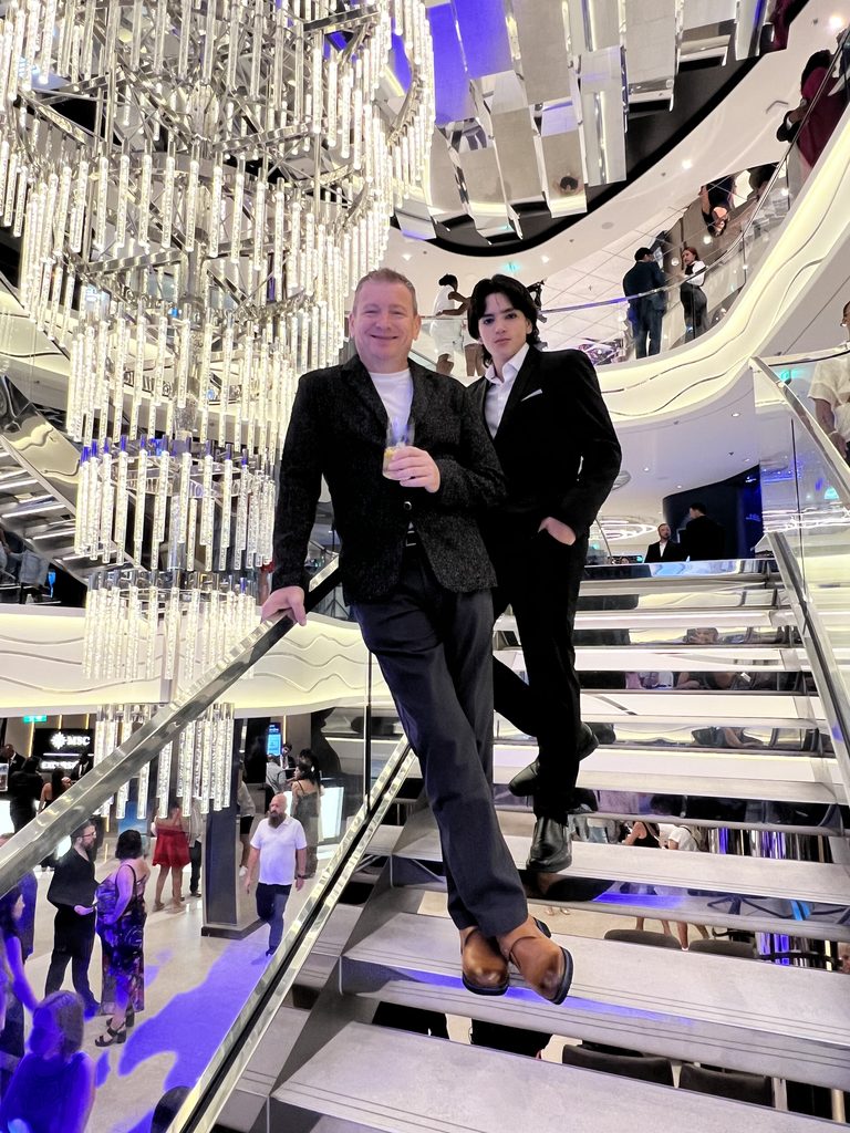Two people in black suits standing on a lit staircase on the ship