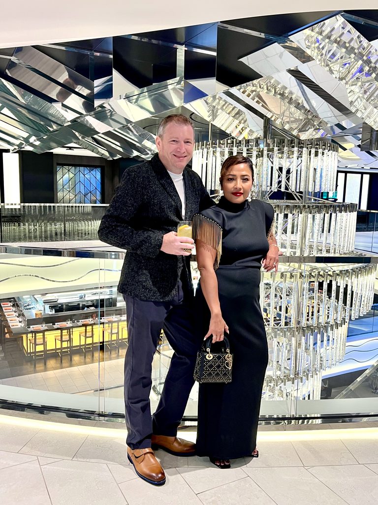 Couple in formal black outfits posing under a crystal sculpture on the ship