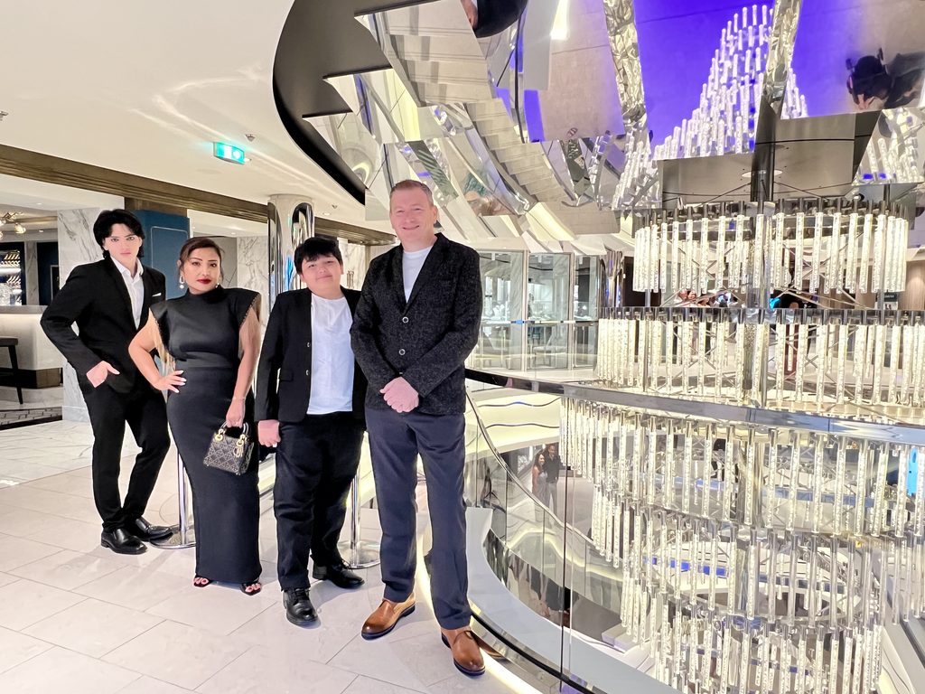 Four people in formal black outfits in the ship atrium beside a crystal staircase