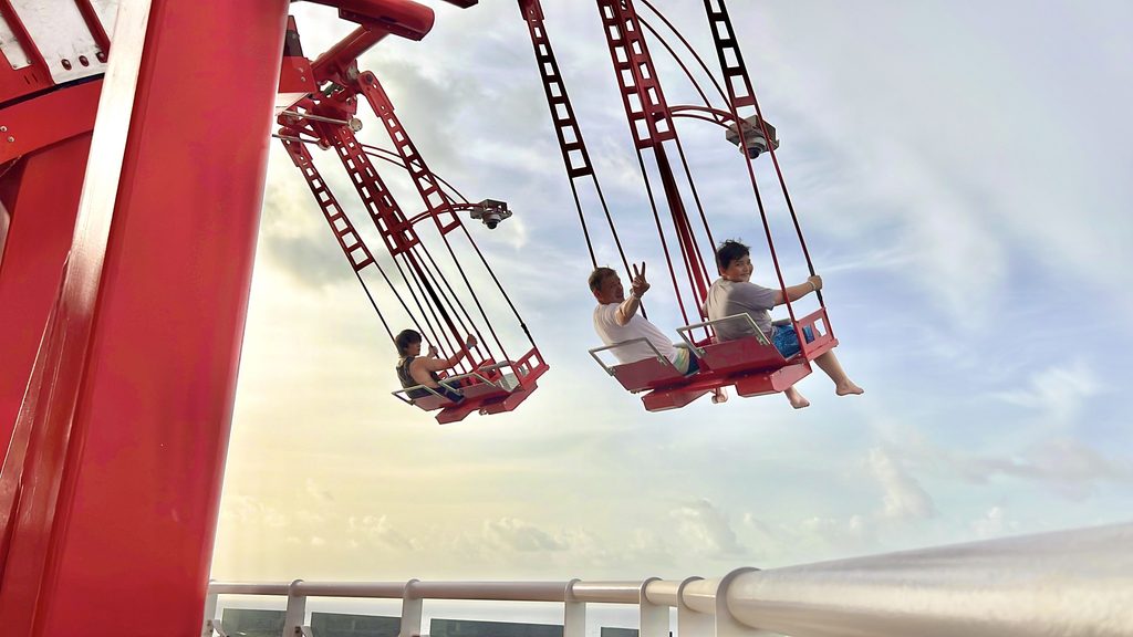 Two people riding a swing ride high above the ocean on a ship