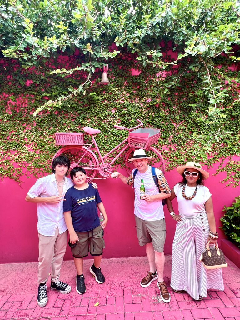 Family posing in front of a pink wall with a bicycle planter
