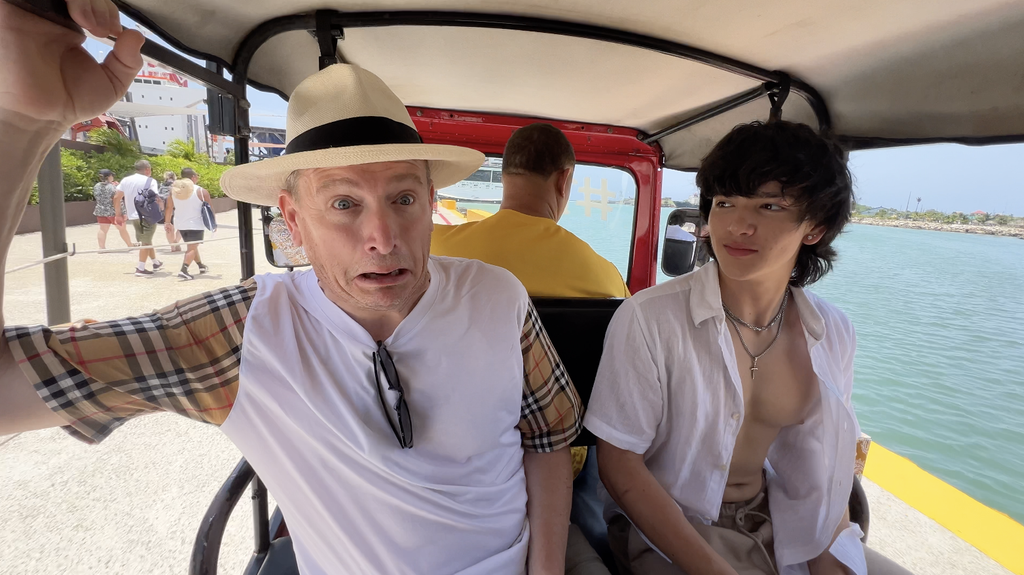 Two people riding in an open-sided vehicle beside the water