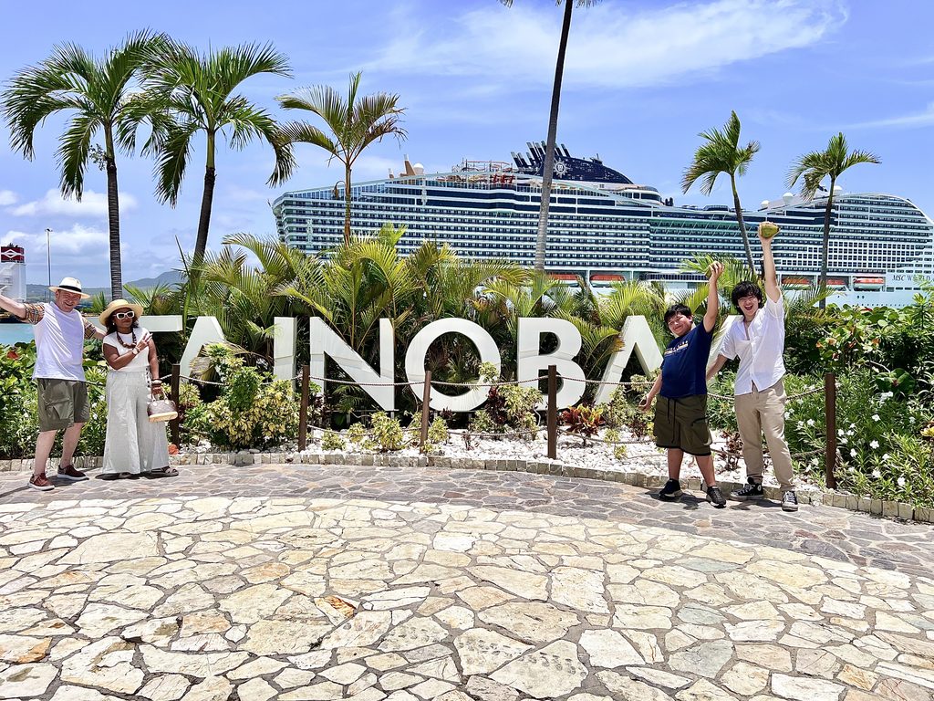 Family posing at the Taino Bay sign with a cruise ship behind palm trees