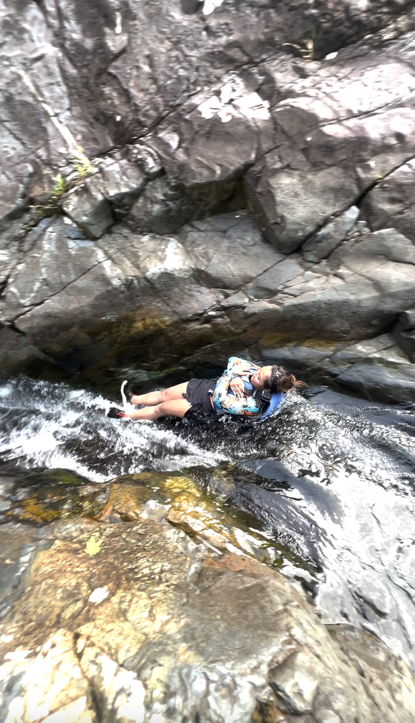 Person lying on a mossy rock slide with water flowing around them