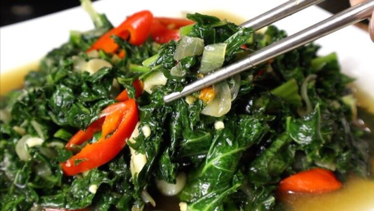 Sauteed kale with garlic and red chili in a bowl, held with chopsticks
