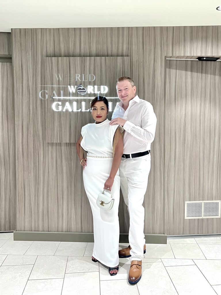 Couple in white outfits posing beside a wall sign on the ship
