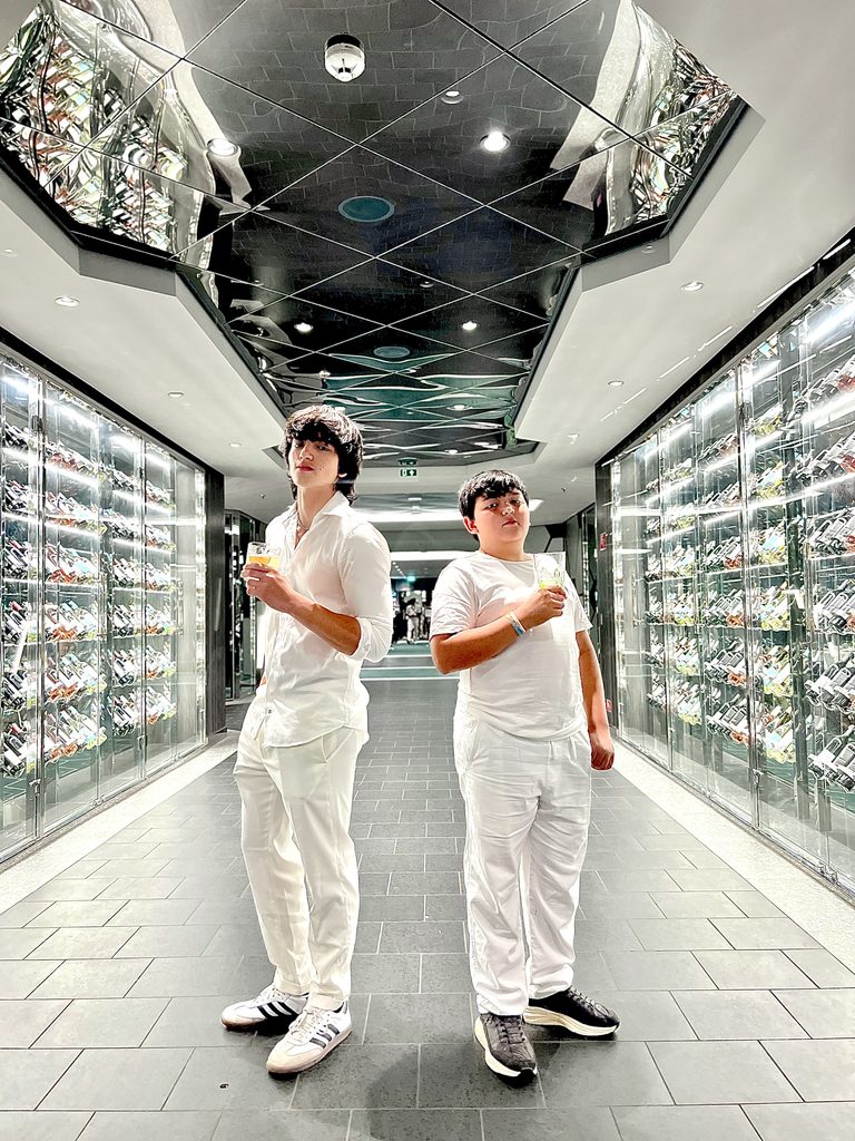 Two boys in white outfits standing in a mirrored ship corridor